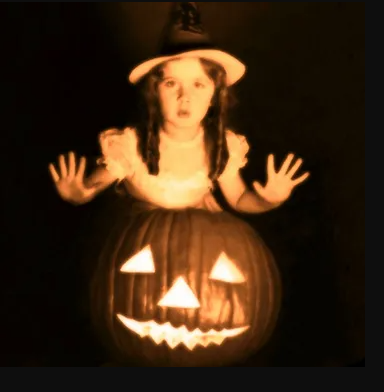 Sepia toned picture of a young girl standing behind a jack o' lantern