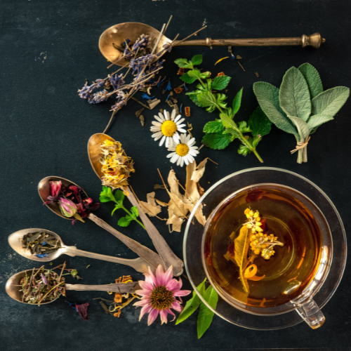 Cup of tea surrounded by spoons, herbs, and loose tea leaves
