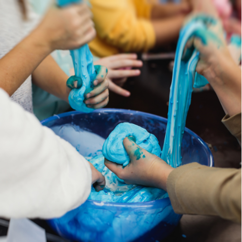Several hands playing with a bowl of blue slime