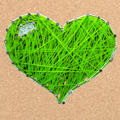 Green heart made of yarn over a corkboard background