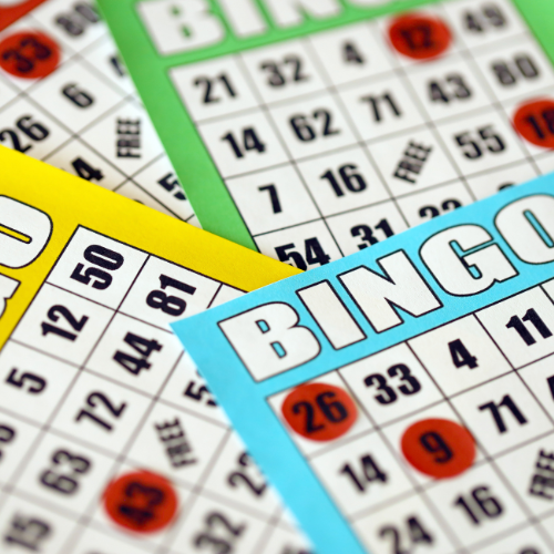 Image of multiple colorful (blue, yellow, and green) Bingo cards with red chips on a few of the numbers.
