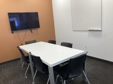 Image of conference room with rectangular table, 6 chairs, wall-mounted white board and television monitor