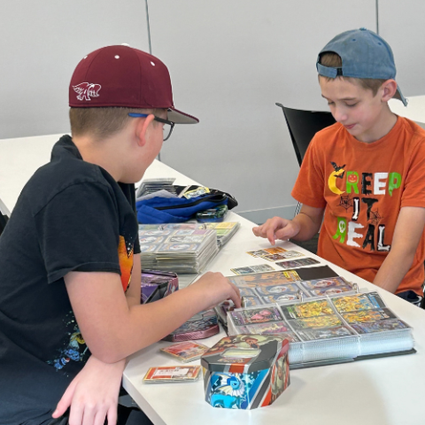 2 teens sitting around a table covered in Pokémon Cards