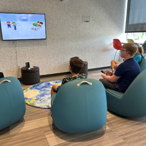 Teens sitting in chairs, playing a Mario video game