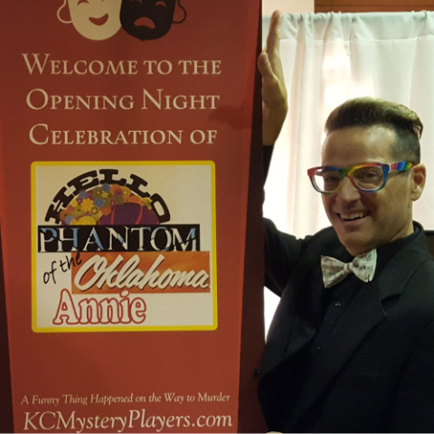 A man in glasses and a bowtie next to a Broadway show poster
