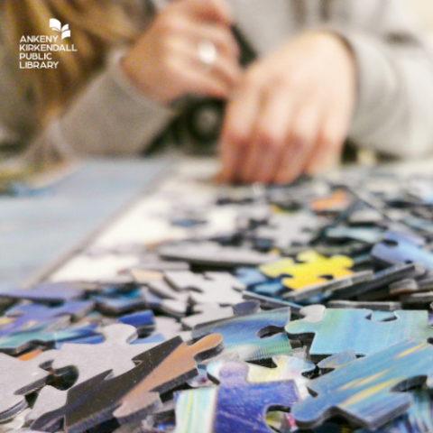 Photo of puzzle pieces and a woman's hands in the distance