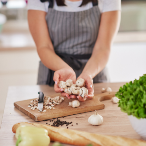 A teen in an apron cutting vegetables on a cutting board