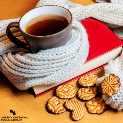 A mug wrapped in a scarf on top of a book with cookies beside it