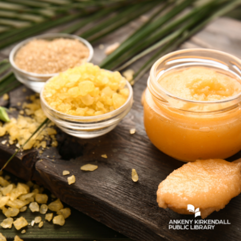 Sugar scrub surrounded by greenery with a bowl of sugar and wooden spoon with sugar scrub