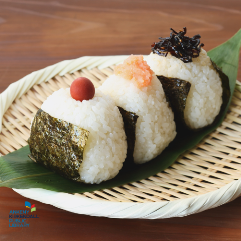 Wicker plate of onigiri topped with a tomato, bonito flakes, and konbu
