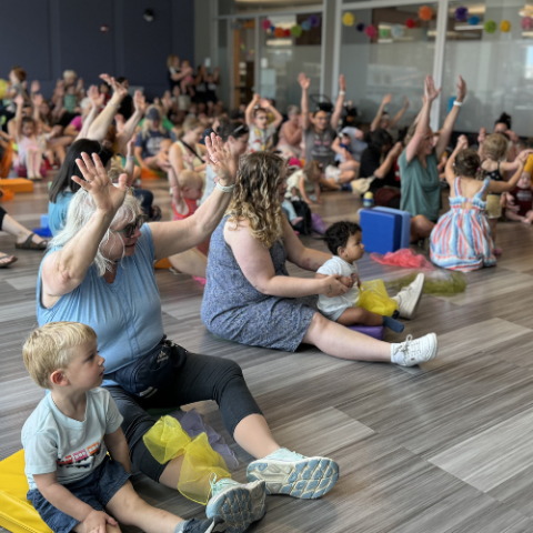 Kids and caregivers are dancing to music in the Children's Program Room.