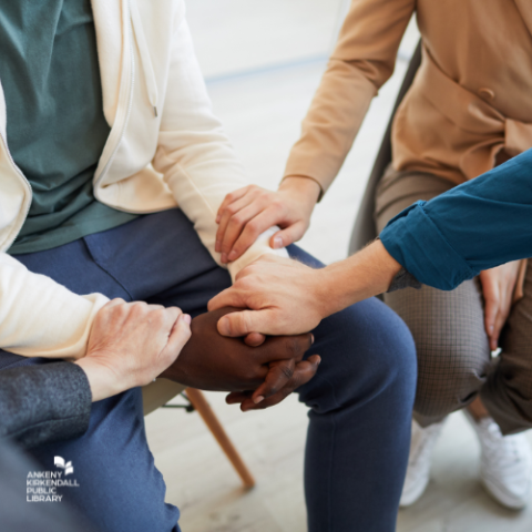 A group of people sitting in a circle and holding hands with the library logo in the bottom left corner