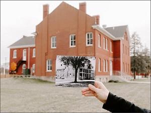 Image of hand holding an old photograph of Ft. Des Moines in front of the current building