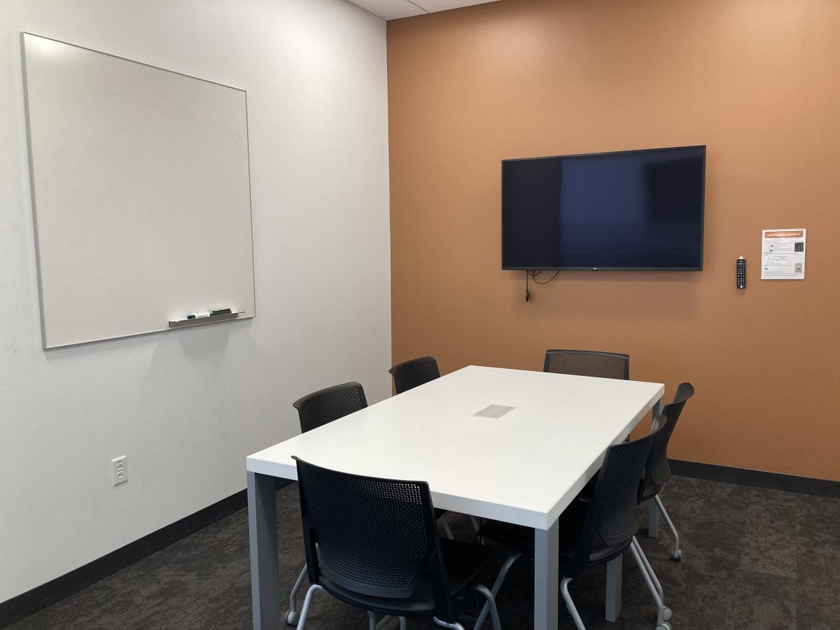 Image of Conference Room with rectangular table, 6 chairs; mounted television; and white board on wall