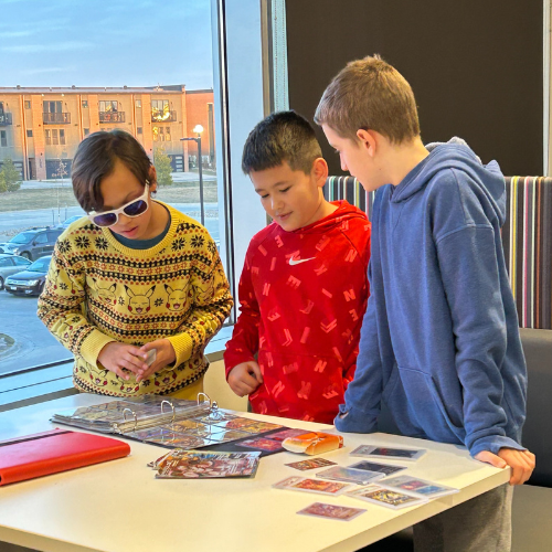 3 teens standing around a table of Pokémon cards