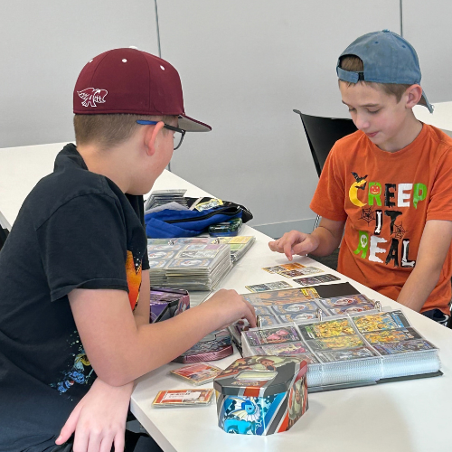 2 teens sitting around a table of Pokémon cards