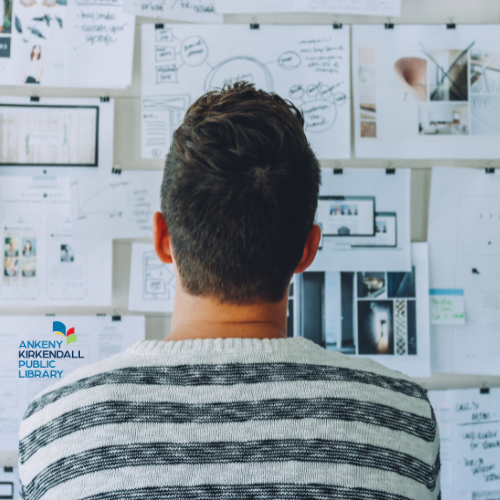 Photo of a man looking at a board with several pieces of paper pinned to it