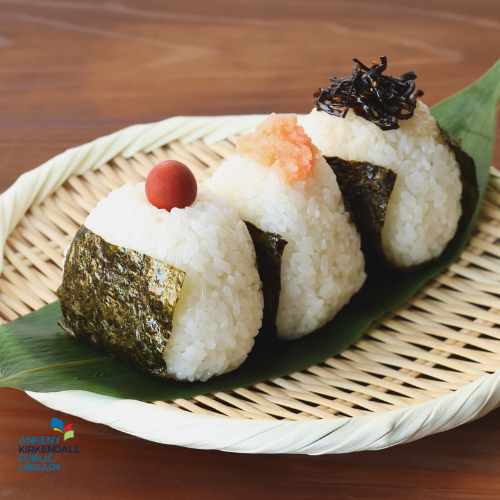 Wicker plate of onigiri topped with a tomato, bonito flakes, and konbu