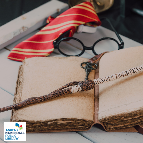 Blank leatherbound journal with a wooden wand and black key on top of it and a red tie and black glasses behind on a desk